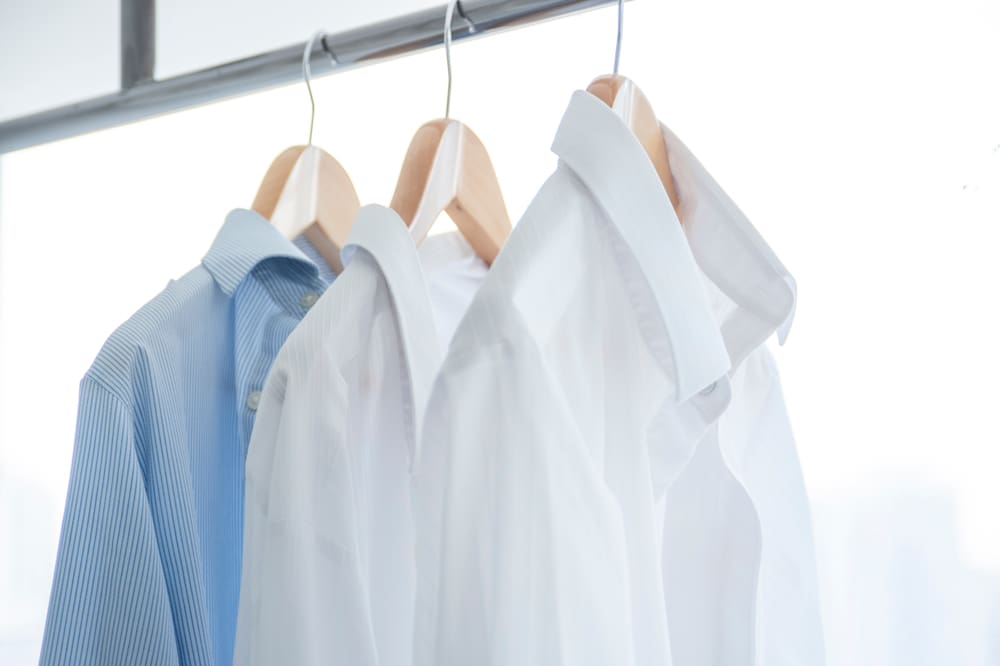 Several neatly pressed shirts hanging on hangers against a bright background.