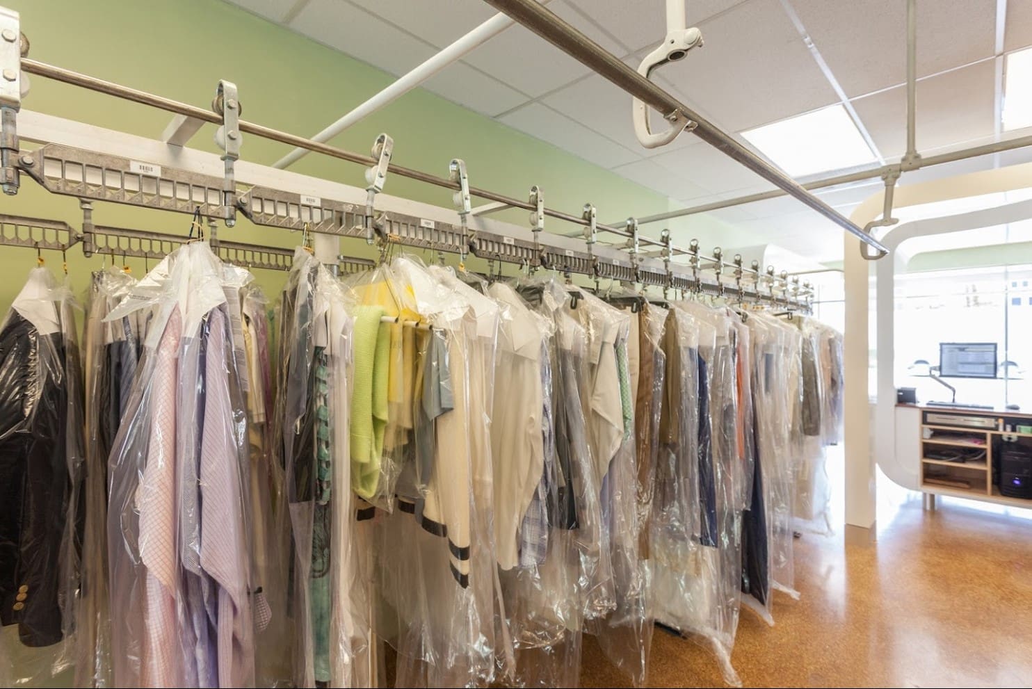 Interior of a dry cleaning shop with various garments hung in clear plastic covers on metal racks.