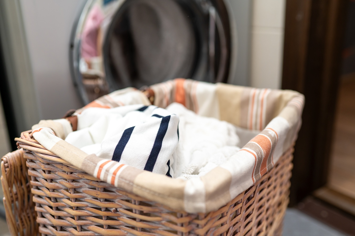 Wicker basket with dirty laundry in front of washing machine